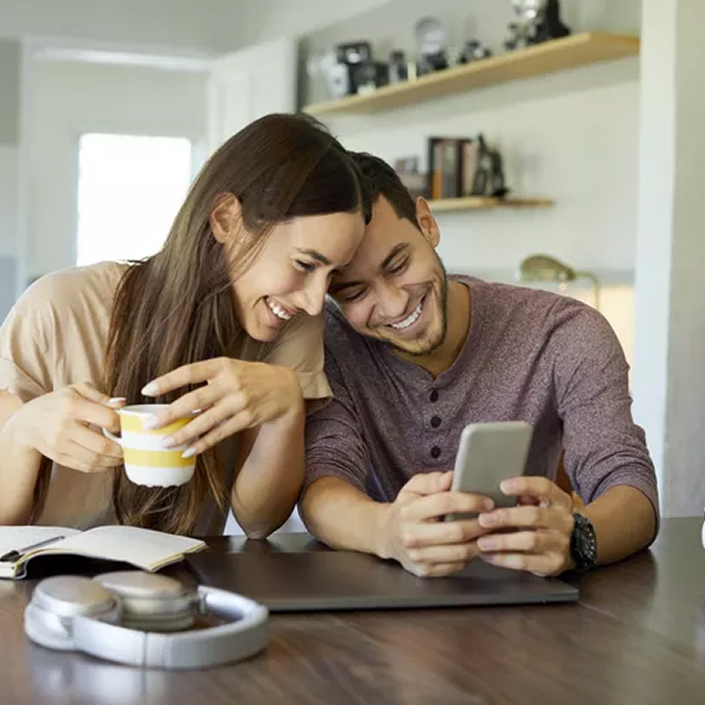 A Fun Couple Looking At Their Phone In The Kitchen