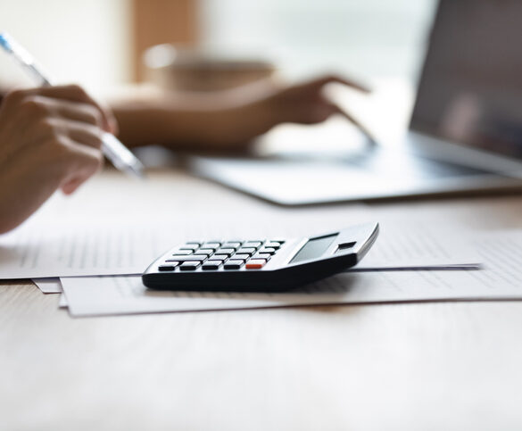 Paying bills. Close up cropped shot of female accountant bookkeeper work at desk on laptop digital calculator. Hands of young woman managing financial papers planning expenses providing payment online