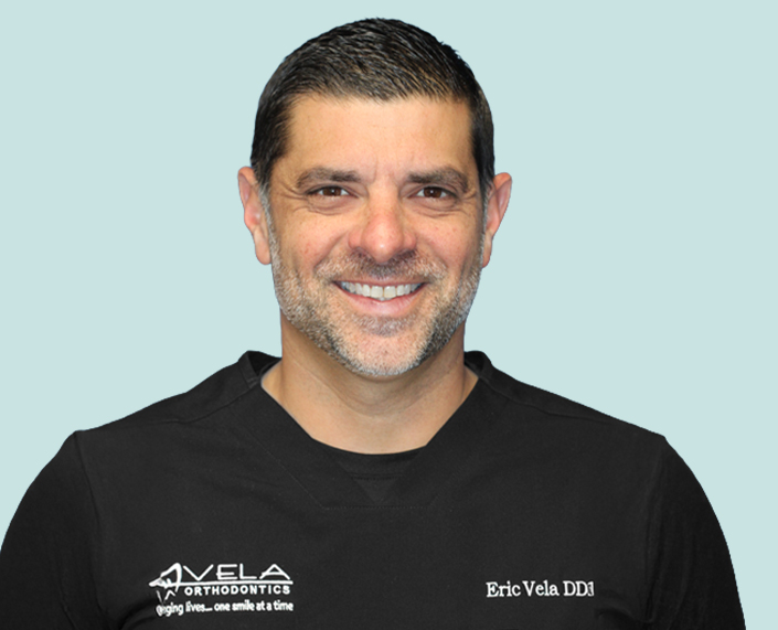 Portrait Of Dr Eric Vela In Front Of A Light Teal Background